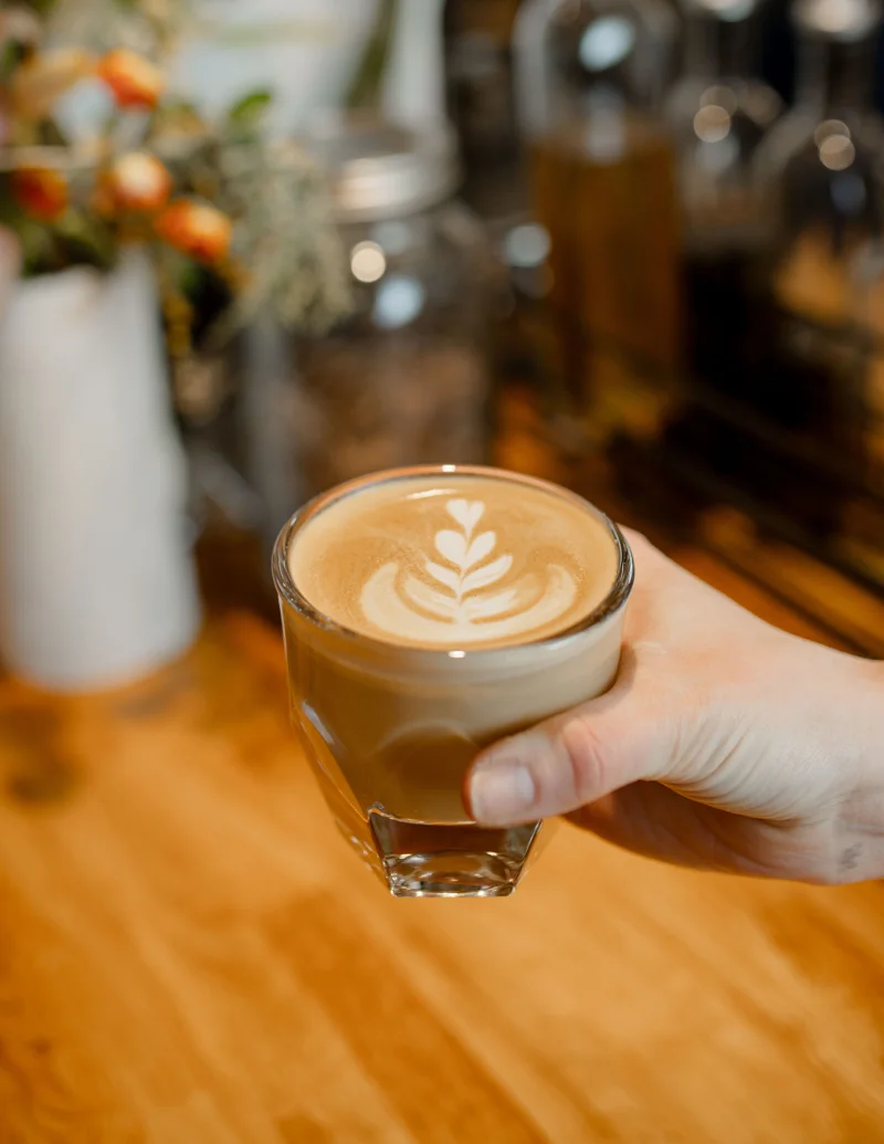 A freshly poured latte held over the wooden coffee bar